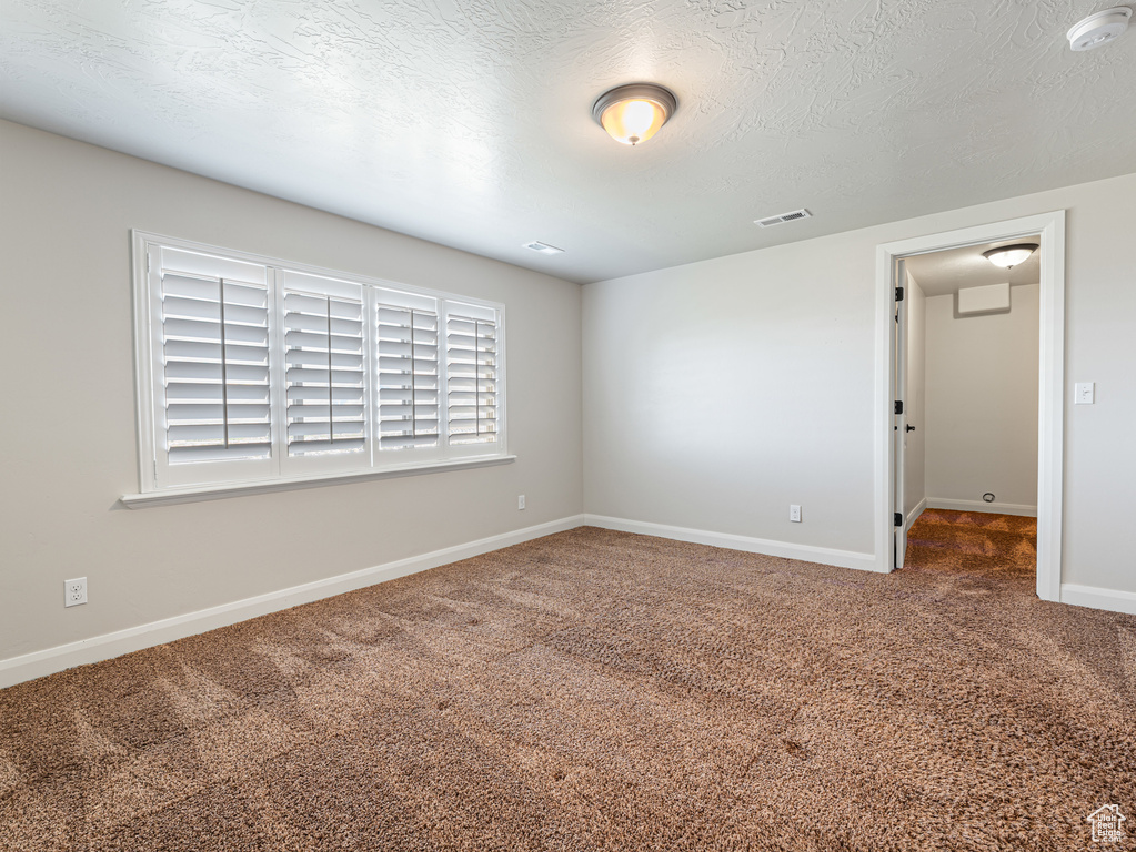 Spare room with a textured ceiling, visible vents, baseboards, and carpet floors
