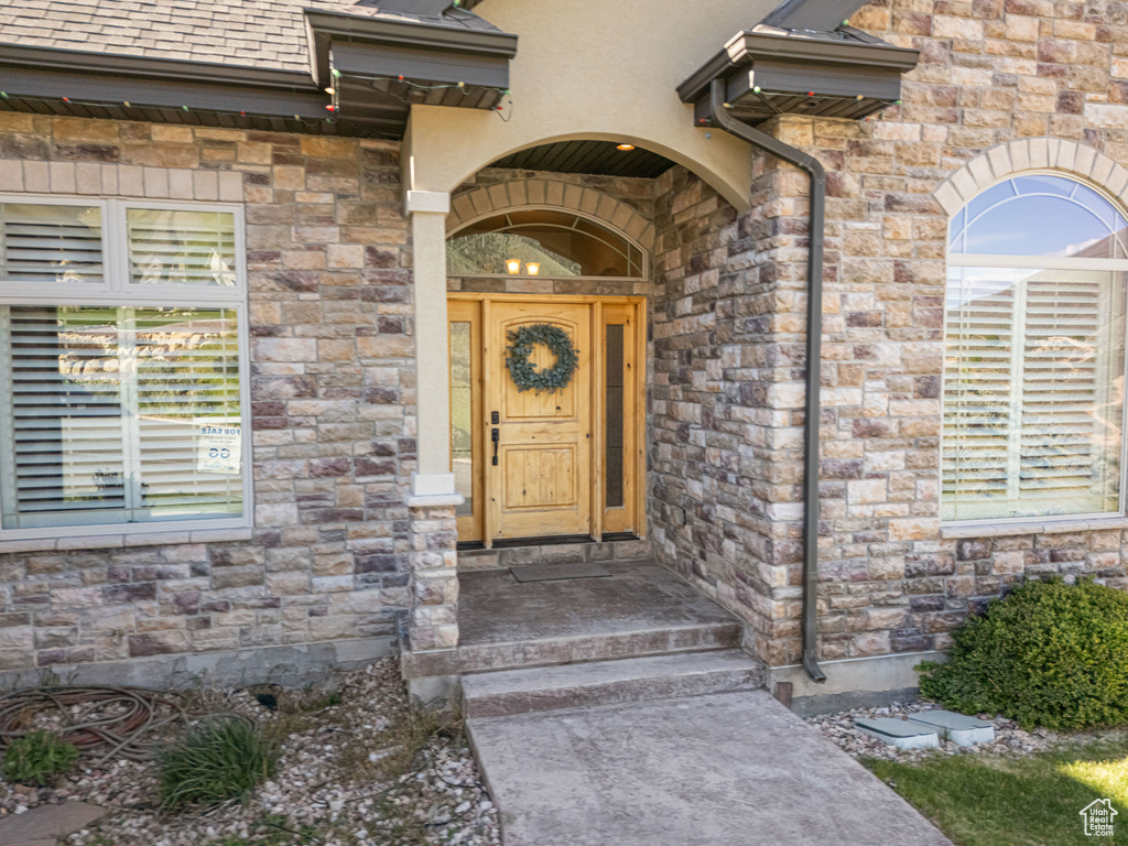 View of exterior entry featuring roof with shingles and stone siding