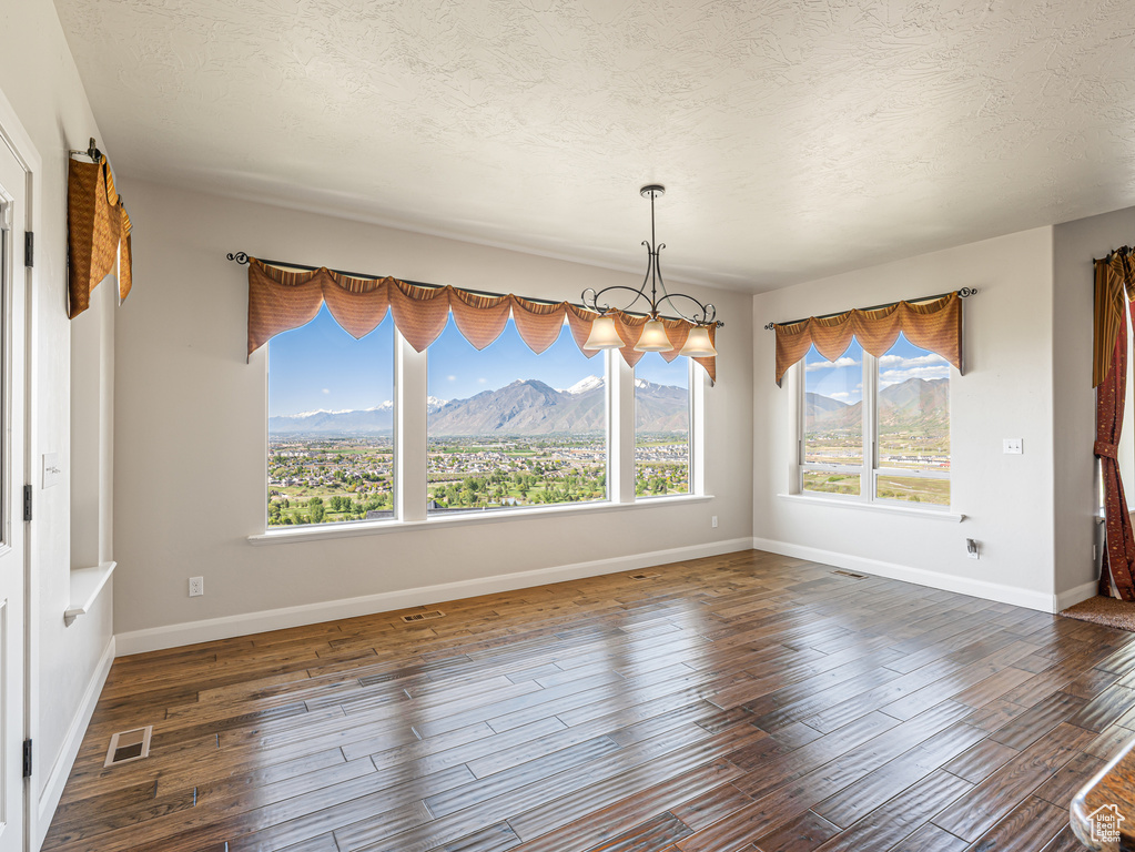 Unfurnished dining area featuring a mountain view, wood finished floors, a textured ceiling, visible vents, and baseboards
