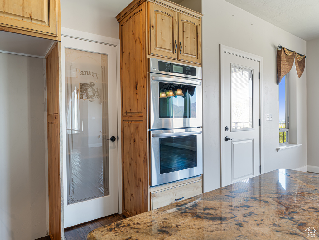 Kitchen with dark wood finished floors, dark stone counters, and stainless steel double oven
