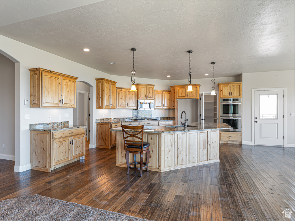 Kitchen featuring baseboards, a sink, arched walkways, stainless steel appliances, and a large island with sink