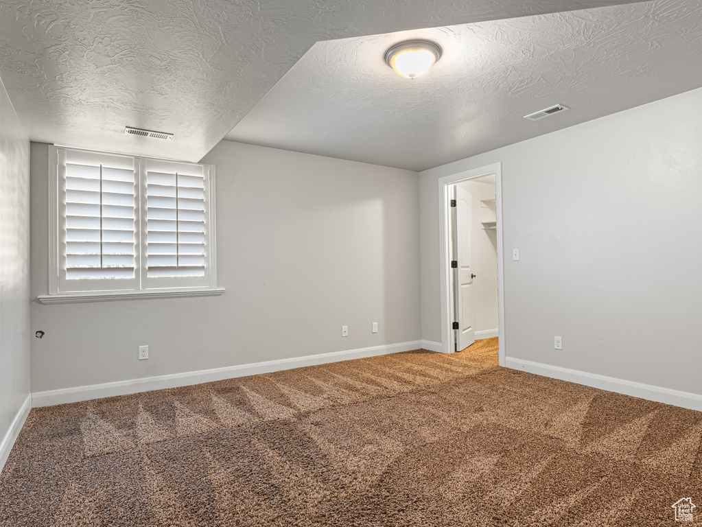 Carpeted spare room with baseboards, visible vents, and a textured ceiling