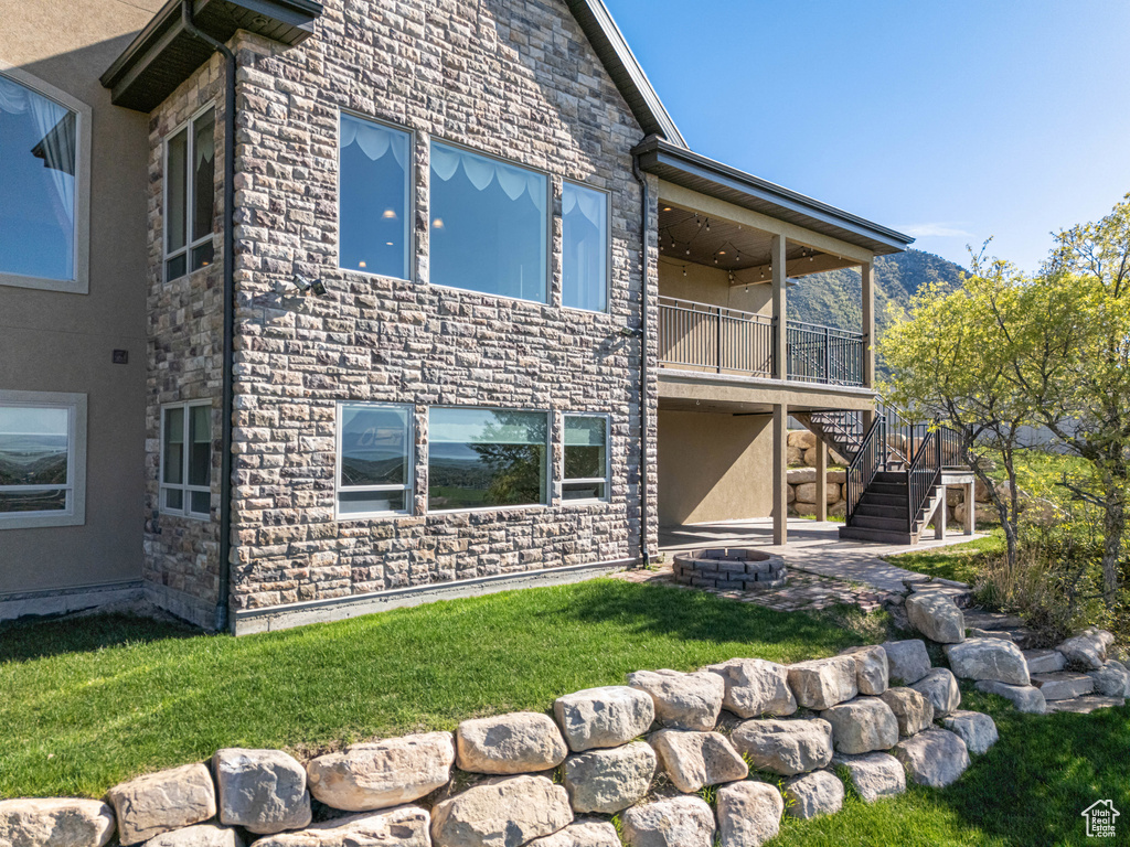 Back of property featuring stone siding, a fire pit, stucco siding, stairway, and a yard