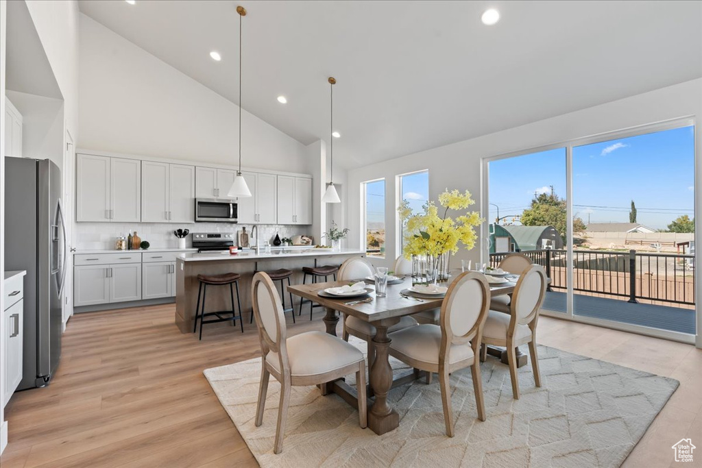 Dining area with light hardwood / wood-style floors and high vaulted ceiling