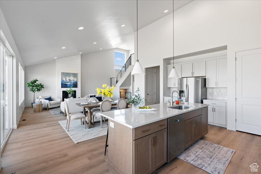 Kitchen featuring sink, decorative light fixtures, white cabinetry, stainless steel appliances, and light hardwood / wood-style floors