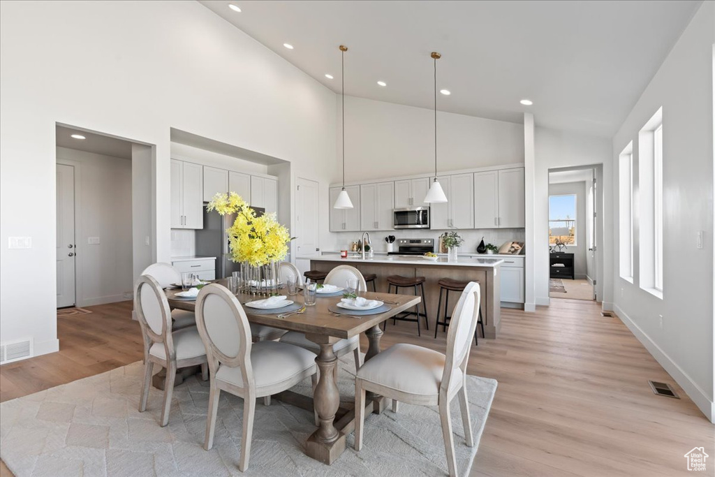 Dining space with sink, light hardwood / wood-style flooring, and high vaulted ceiling