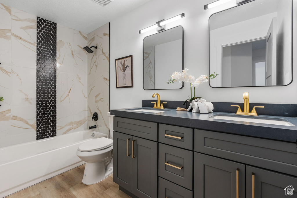 Full bathroom with vanity, tiled shower / bath combo, toilet, and hardwood / wood-style flooring