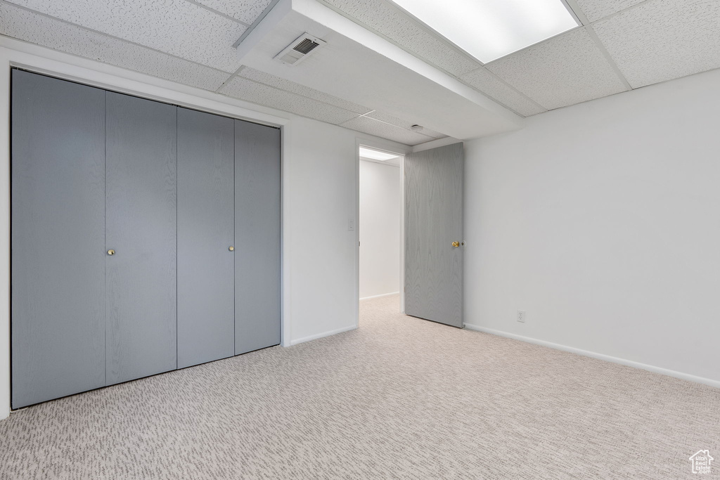 Unfurnished bedroom featuring light colored carpet, a closet, and a paneled ceiling