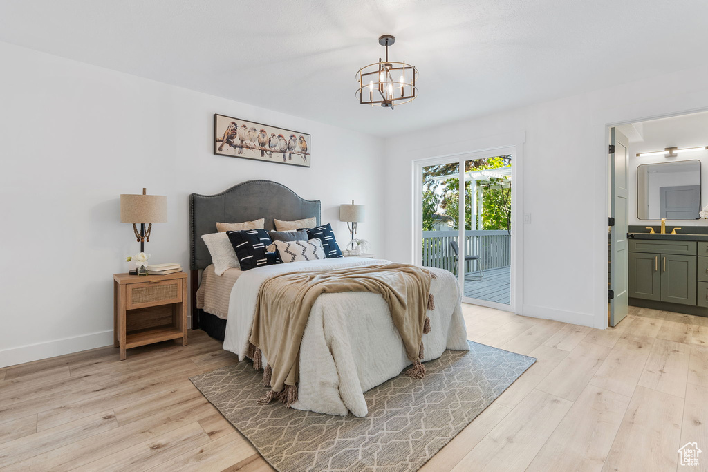 Bedroom with light wood-type flooring, access to outside, ensuite bath, sink, and a notable chandelier