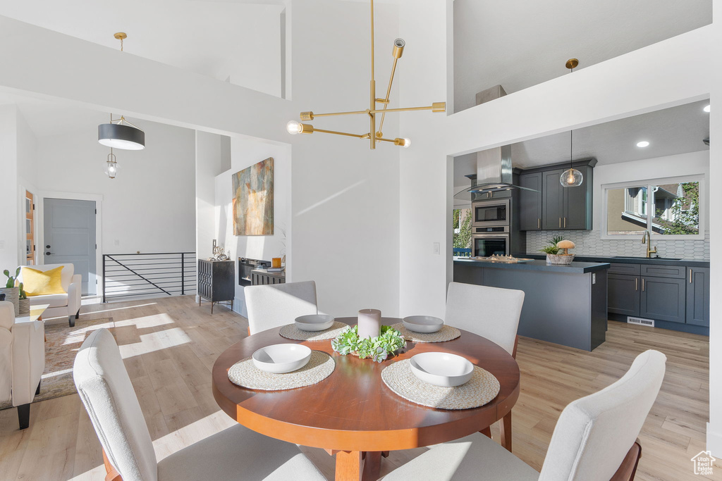 Dining area featuring a notable chandelier, light hardwood / wood-style flooring, a towering ceiling, and sink