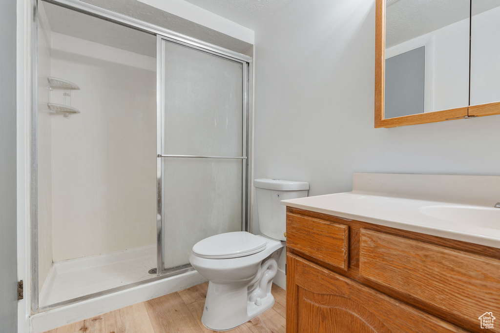 Bathroom with a shower with shower door, vanity, a textured ceiling, toilet, and hardwood / wood-style floors