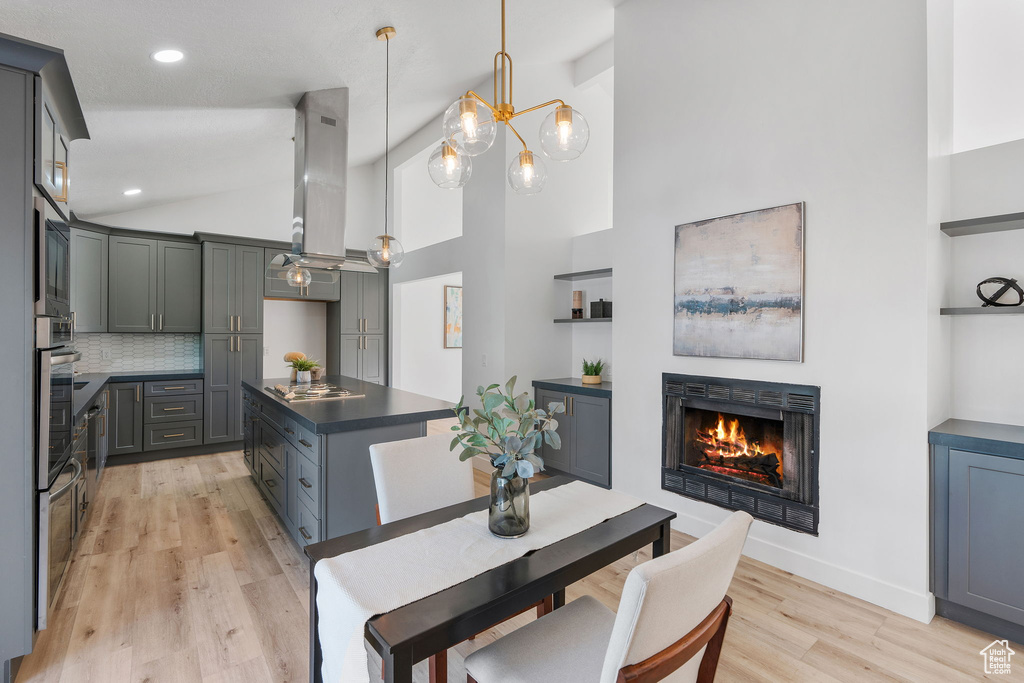 Kitchen featuring island range hood, pendant lighting, light wood-type flooring, and high vaulted ceiling