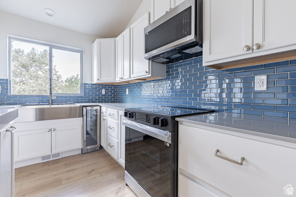 Kitchen with appliances with stainless steel finishes, light wood-type flooring, wine cooler, and white cabinets