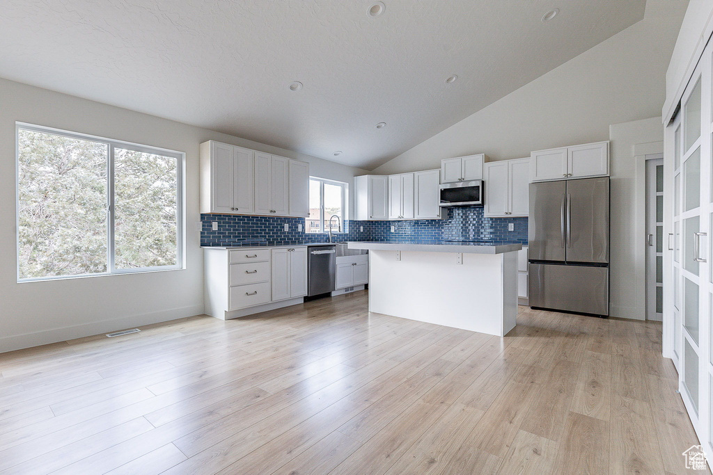 Kitchen featuring light wood-type flooring, white cabinetry, a kitchen island, high vaulted ceiling, and stainless steel appliances