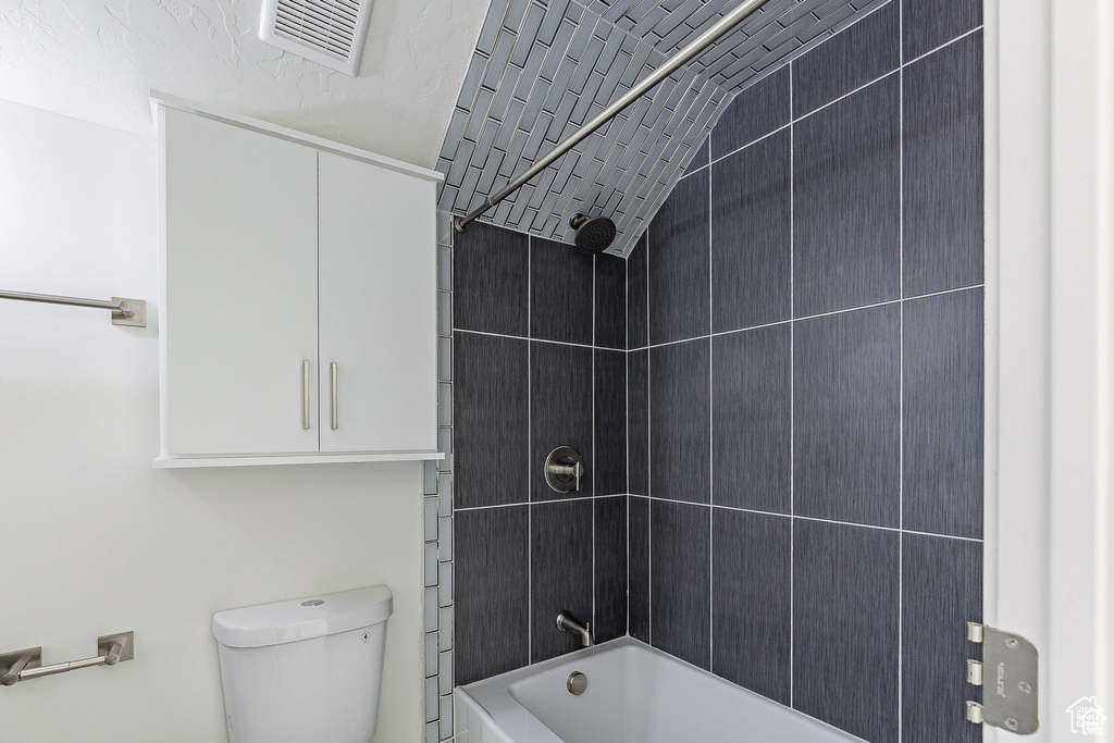 Bathroom with vaulted ceiling, tiled shower / bath combo, and toilet