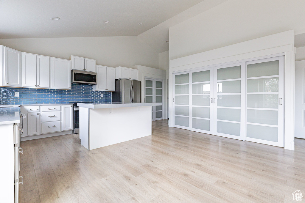 Kitchen with stainless steel appliances, white cabinetry, light wood-type flooring, and a kitchen island