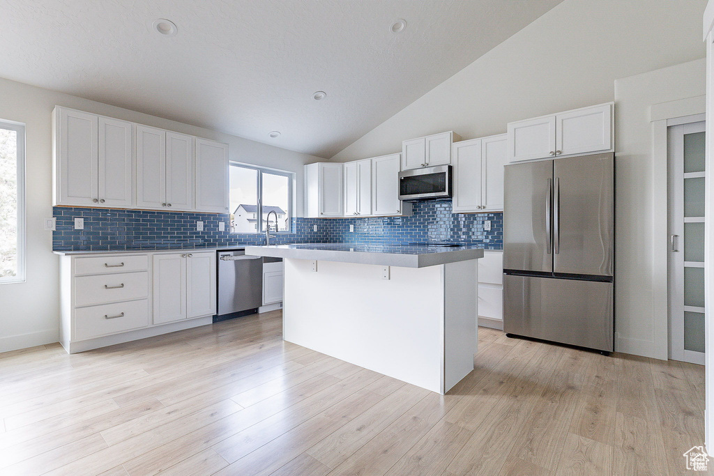 Kitchen with light hardwood / wood-style floors, appliances with stainless steel finishes, white cabinetry, and a center island