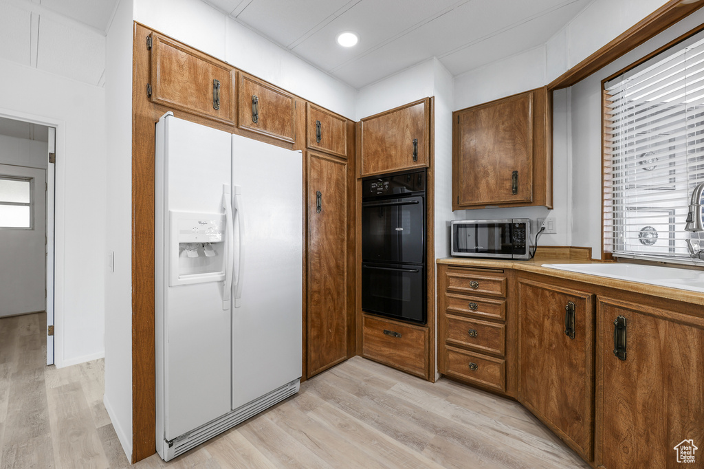 Kitchen featuring light wood-type flooring, white fridge with ice dispenser, black double oven, and sink