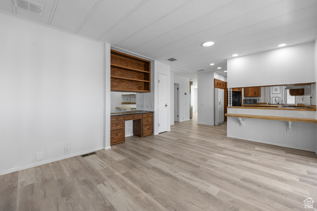 Kitchen featuring a breakfast bar, light wood-type flooring, built in desk, white fridge with ice dispenser, and kitchen peninsula