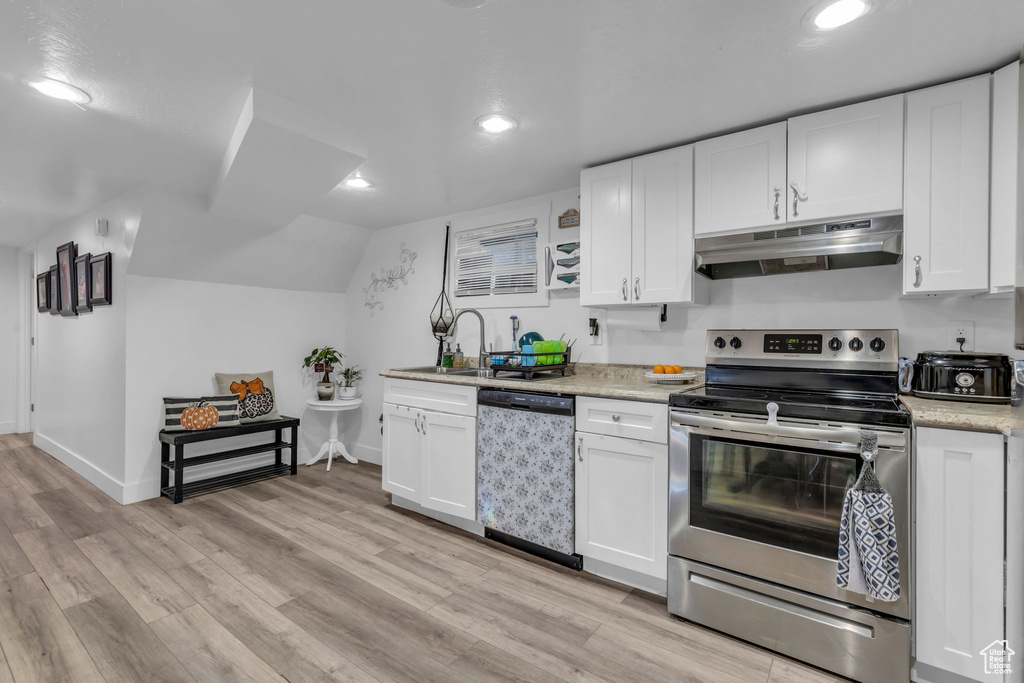 Kitchen with light wood-type flooring, vaulted ceiling, stainless steel appliances, and white cabinets