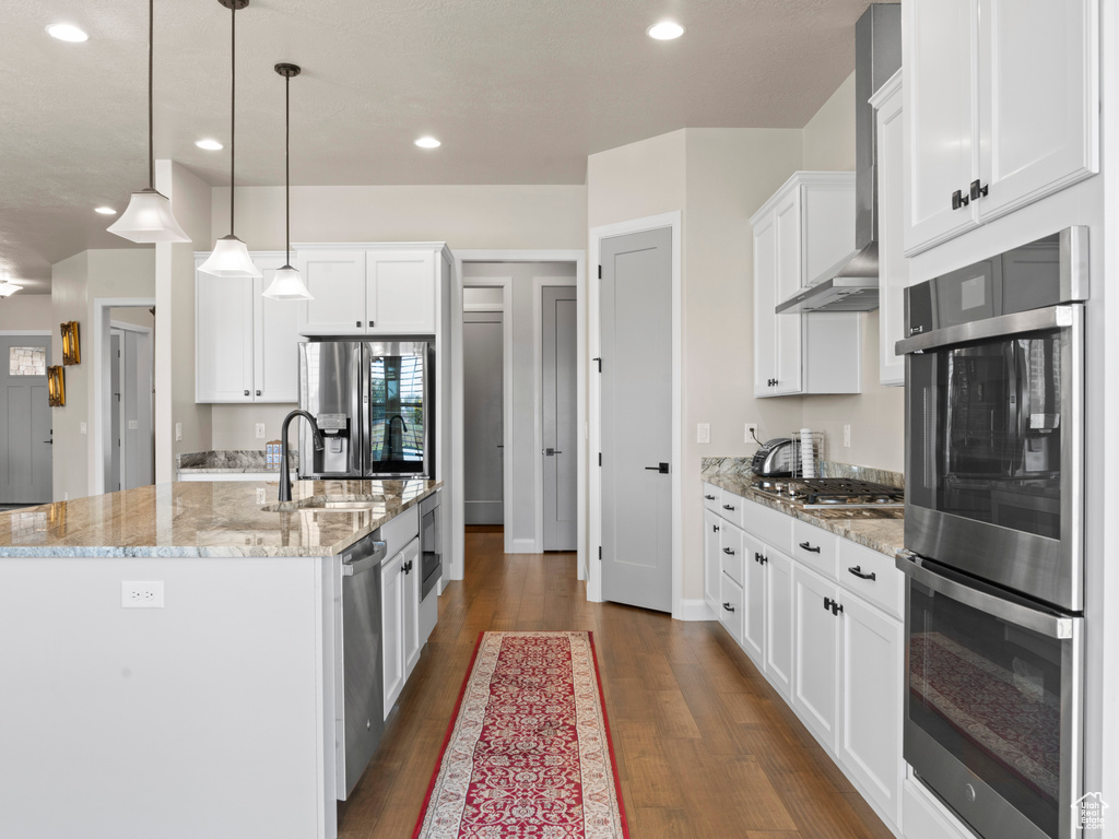 Kitchen with dark hardwood / wood-style floors, sink, white cabinets, wall chimney range hood, and decorative light fixtures