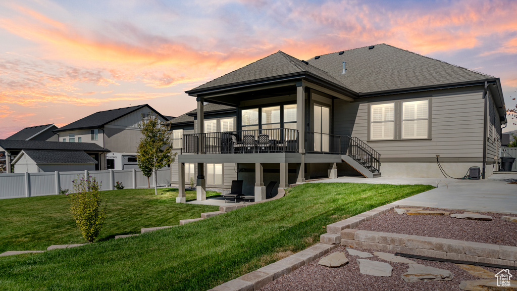 Back house at dusk featuring a lawn and a patio area