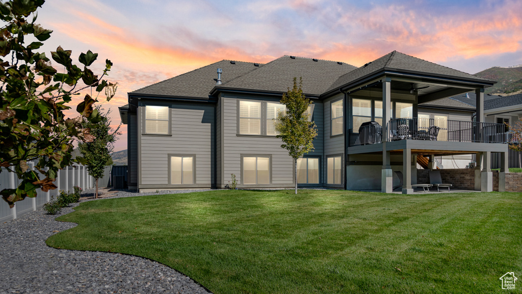 Back house at dusk with a yard, a wooden deck, and a patio area