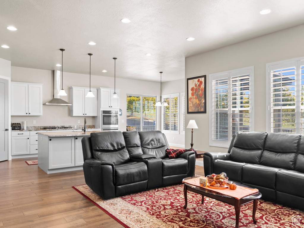 Living room with a notable chandelier, a wealth of natural light, light wood-type flooring, and sink