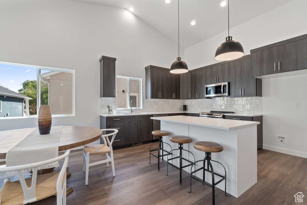 Kitchen featuring decorative light fixtures, backsplash, appliances with stainless steel finishes, dark hardwood / wood-style floors, and a center island