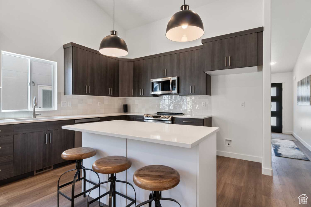 Kitchen with a center island, dark wood-type flooring, hanging light fixtures, decorative backsplash, and appliances with stainless steel finishes