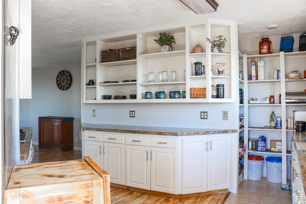 Interior space featuring light wood-type flooring, a textured ceiling, white cabinetry, and light stone countertops