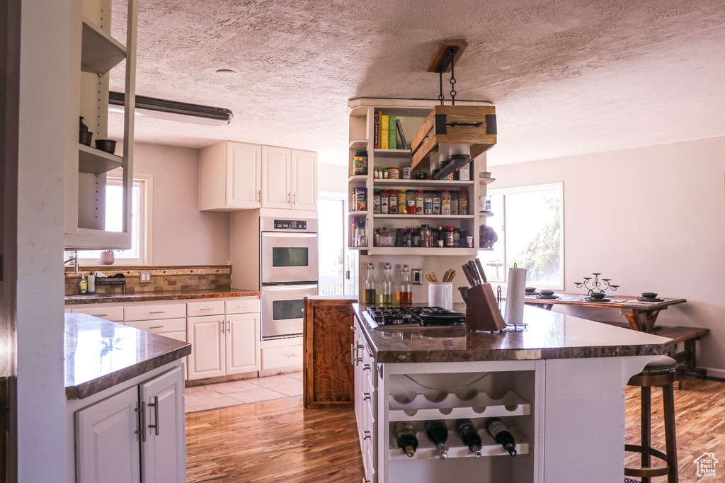 Kitchen with light hardwood / wood-style flooring, white cabinets, a textured ceiling, and appliances with stainless steel finishes