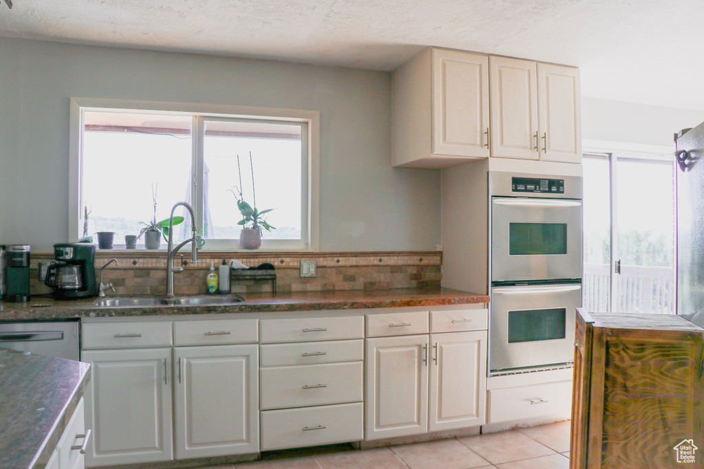 Kitchen featuring light tile patterned floors, double oven, sink, and white cabinetry