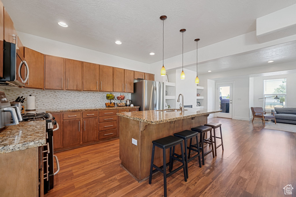 Kitchen with an island with sink, hanging light fixtures, a textured ceiling, appliances with stainless steel finishes, and dark hardwood / wood-style floors