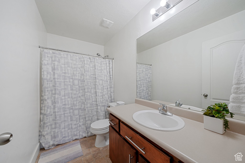 Bathroom featuring curtained shower, a textured ceiling, vanity, and toilet