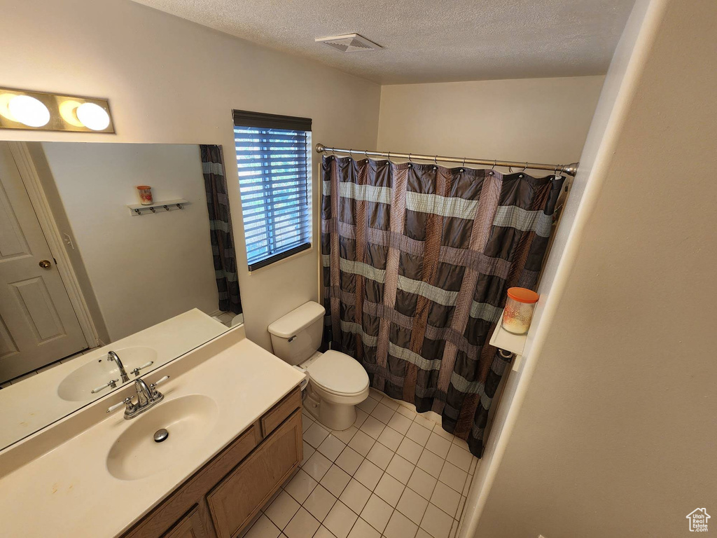 Bathroom with a textured ceiling, tile patterned flooring, vanity, and toilet