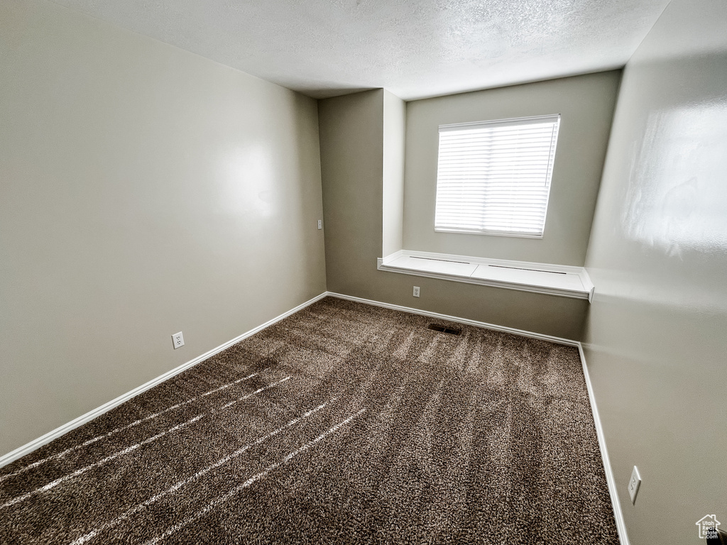 Spare room featuring a textured ceiling and dark colored carpet