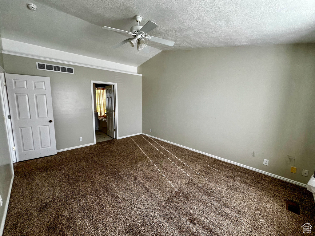 Unfurnished bedroom featuring connected bathroom, lofted ceiling, carpet flooring, a textured ceiling, and ceiling fan