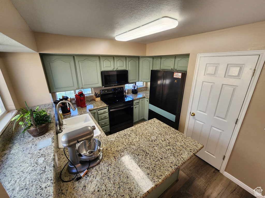 Kitchen with light stone counters, kitchen peninsula, black appliances, green cabinets, and dark hardwood / wood-style flooring