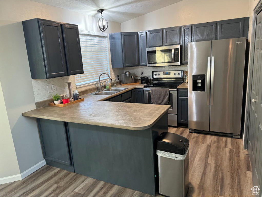 Kitchen featuring sink, kitchen peninsula, appliances with stainless steel finishes, decorative light fixtures, and dark hardwood / wood-style flooring