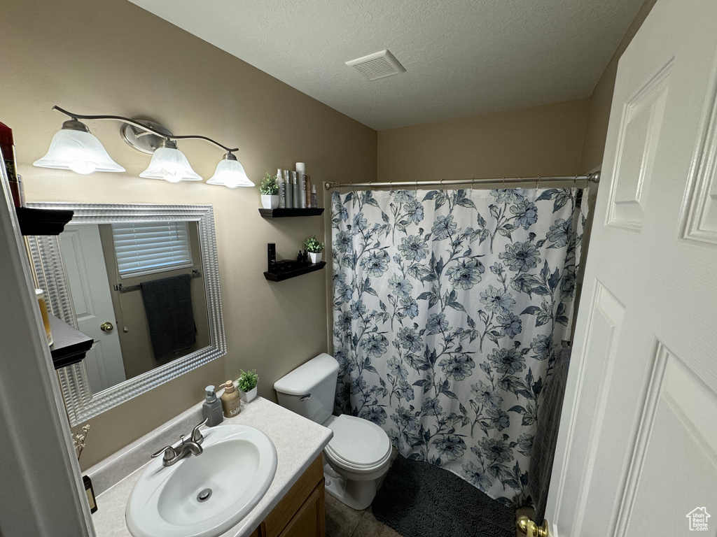 Bathroom with a textured ceiling, curtained shower, vanity, and toilet