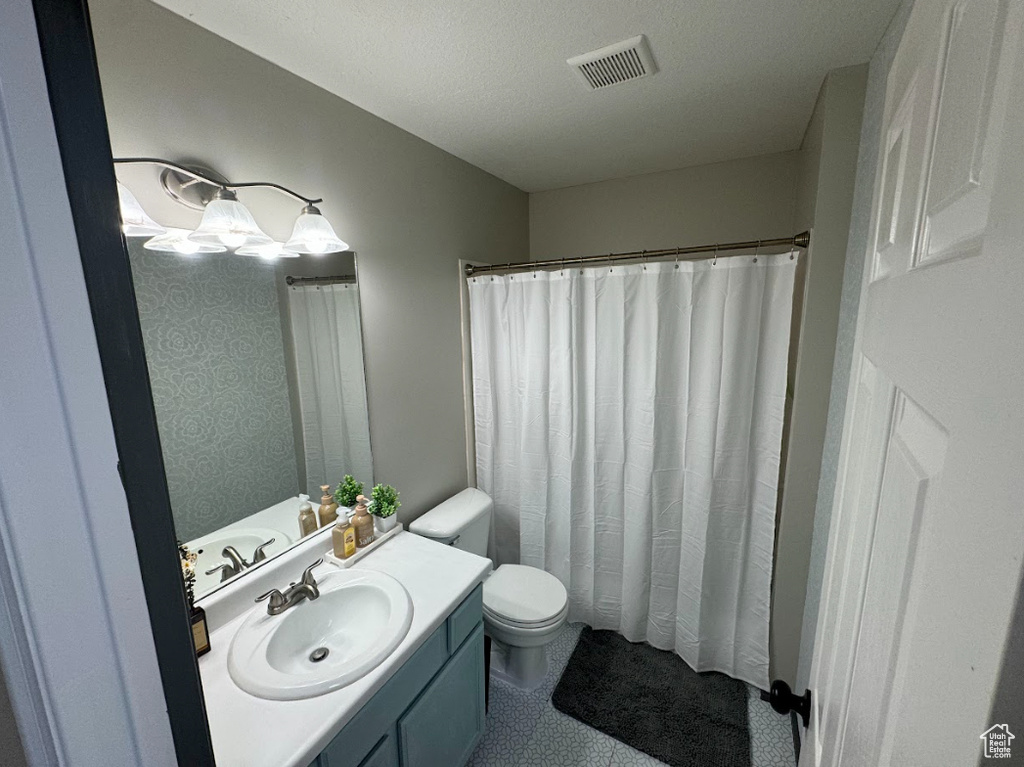 Bathroom with a textured ceiling, curtained shower, vanity, and toilet