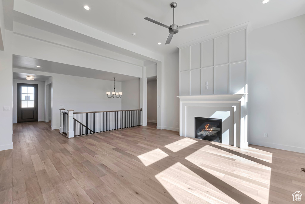 Unfurnished living room featuring light wood-type flooring and ceiling fan with notable chandelier