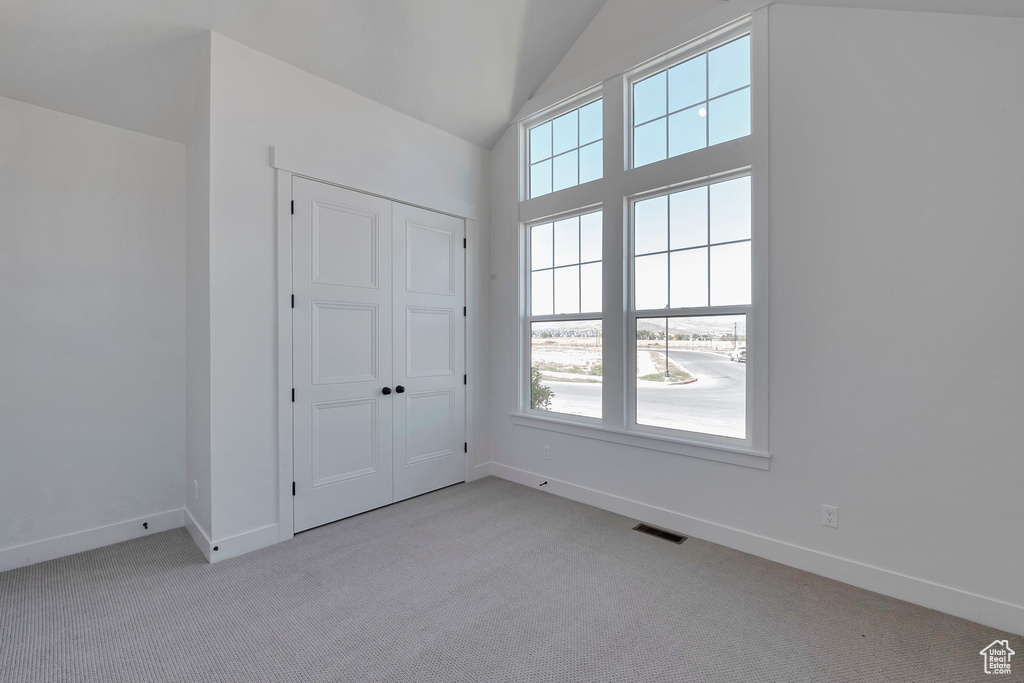 Unfurnished bedroom featuring light carpet, a closet, vaulted ceiling, and multiple windows