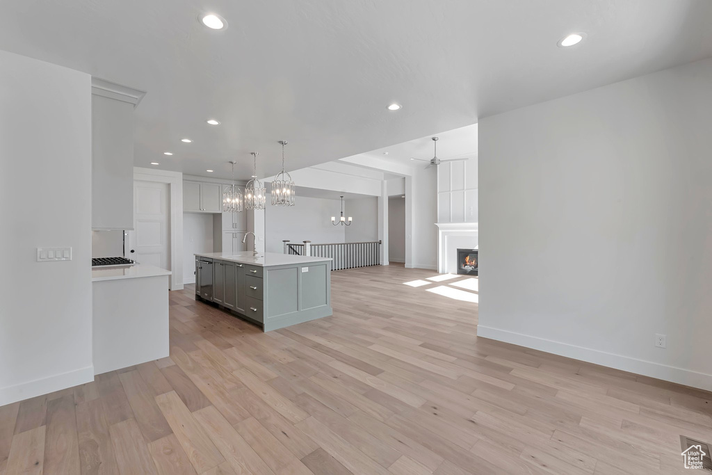 Kitchen featuring light wood-type flooring, sink, decorative light fixtures, a kitchen island with sink, and ceiling fan with notable chandelier