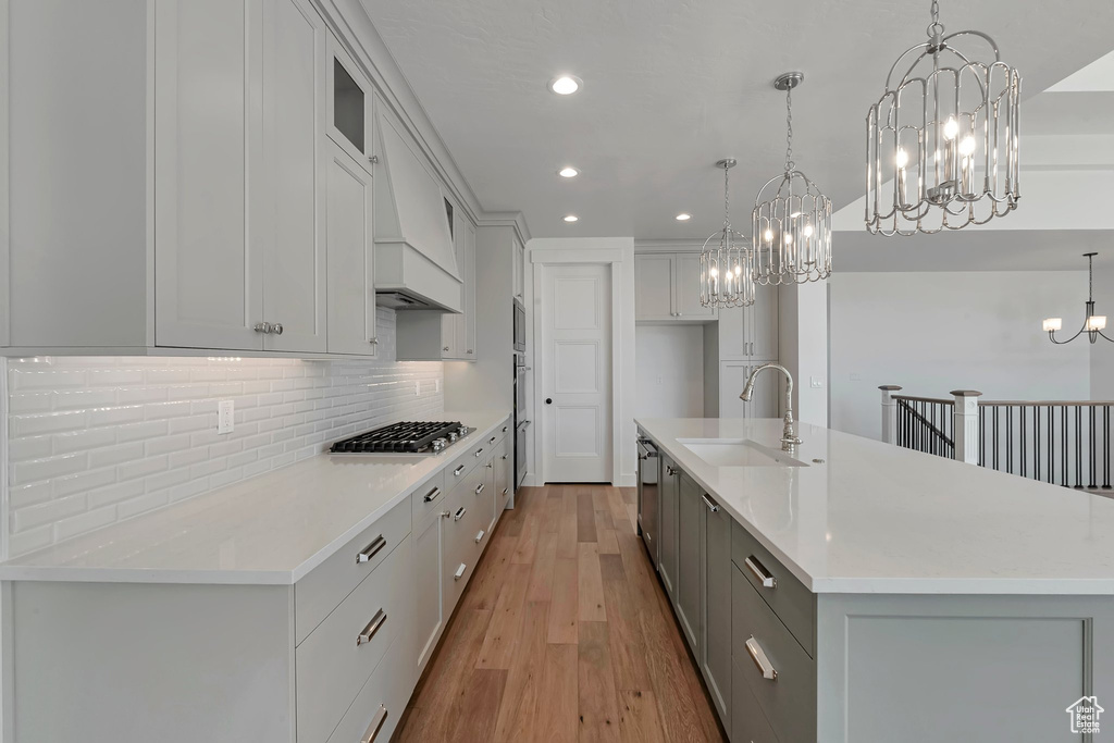 Kitchen featuring pendant lighting, light hardwood / wood-style floors, a large island with sink, sink, and stainless steel appliances