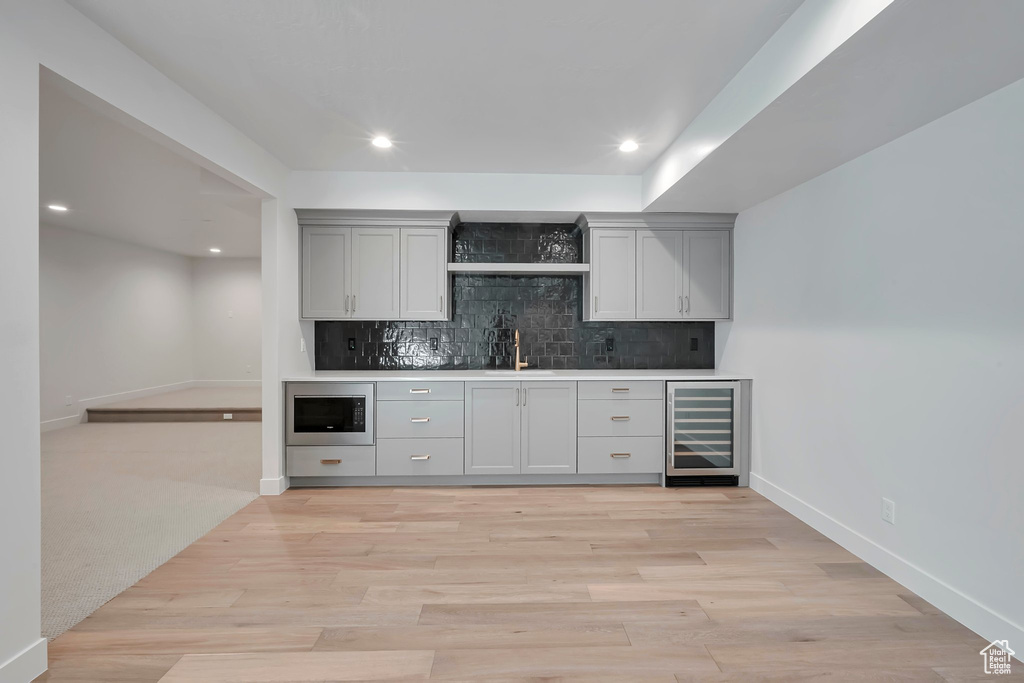 Kitchen with light wood-type flooring, backsplash, gray cabinetry, and beverage cooler