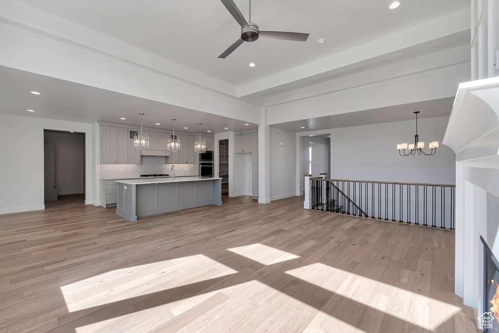 Unfurnished living room with ceiling fan with notable chandelier, light wood-type flooring, and sink