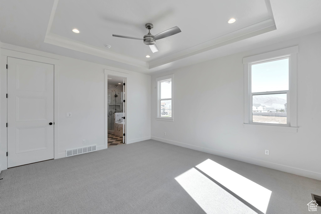 Unfurnished bedroom with a tray ceiling, ceiling fan, light colored carpet, and ensuite bathroom