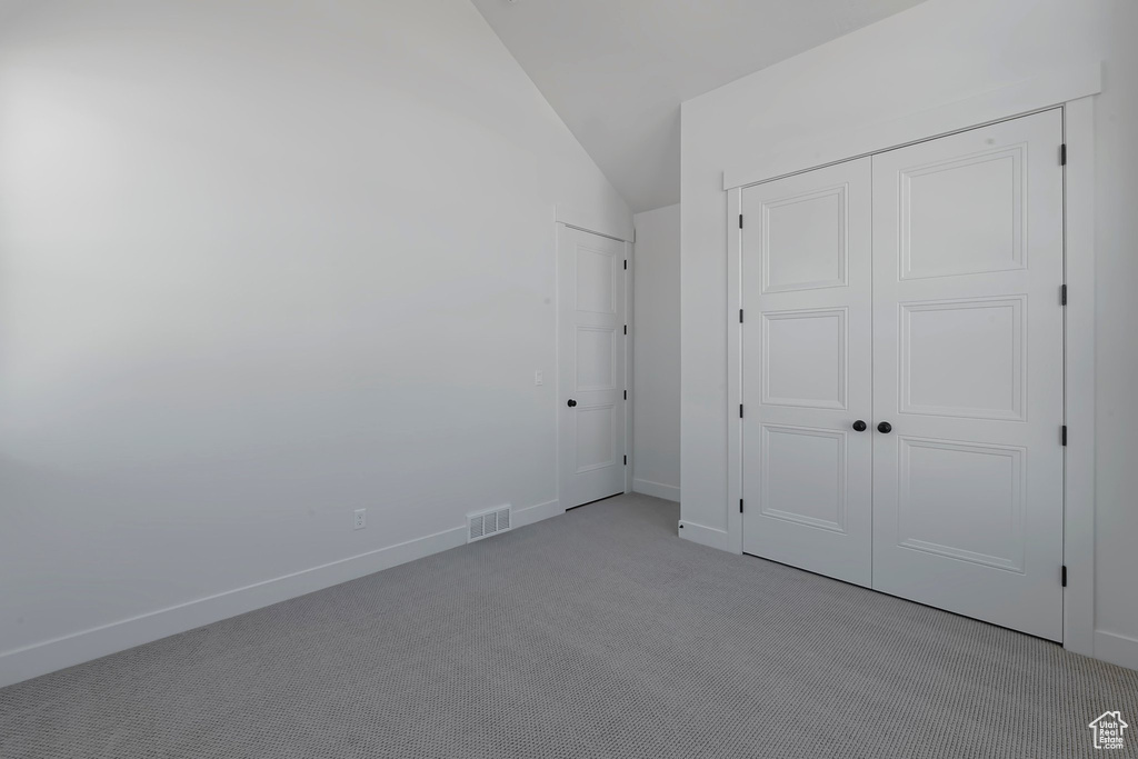 Unfurnished bedroom featuring vaulted ceiling, light colored carpet, and a closet